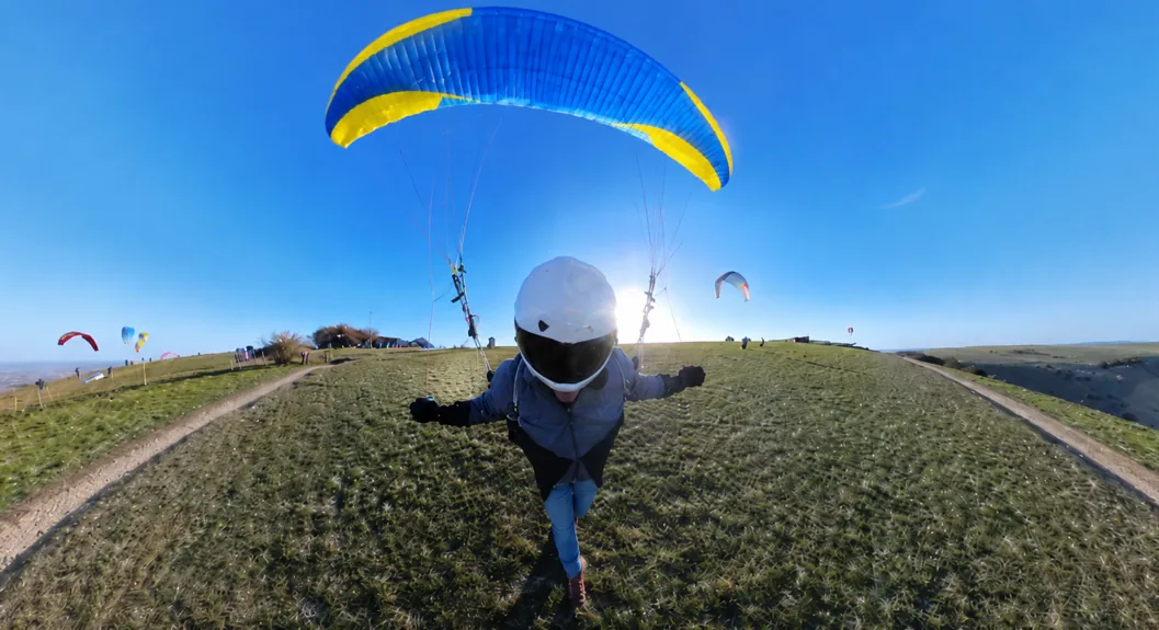 Paragliding student ground handling a blue and yellow wing on a green hillside