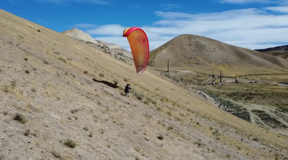 Pilot launching a bright red paraglider on a dry mountain slope