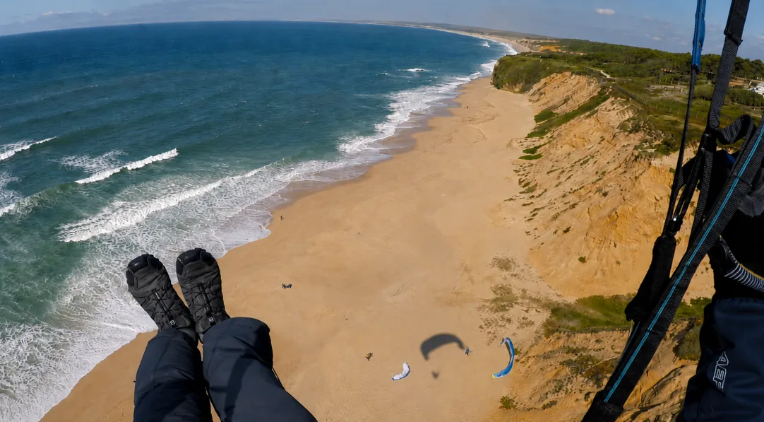 Paraglider soaring over a long golden beach and blue Atlantic during spring in Portugal
