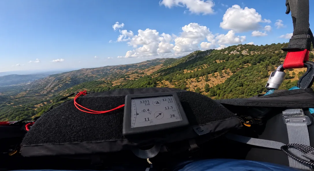 Paragliding variometer mounted on a harness with mountain scenery