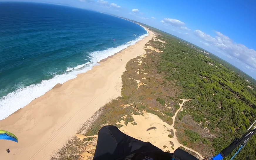 Pilot's view while coastal soaring above a long Atlantic beach and dunes near Sesimbra, Portugal