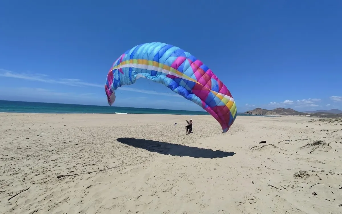 Paragliding ground handling on a wide Atlantic beach in Portugal: pilot controlling a colourful wing in steady sea wind