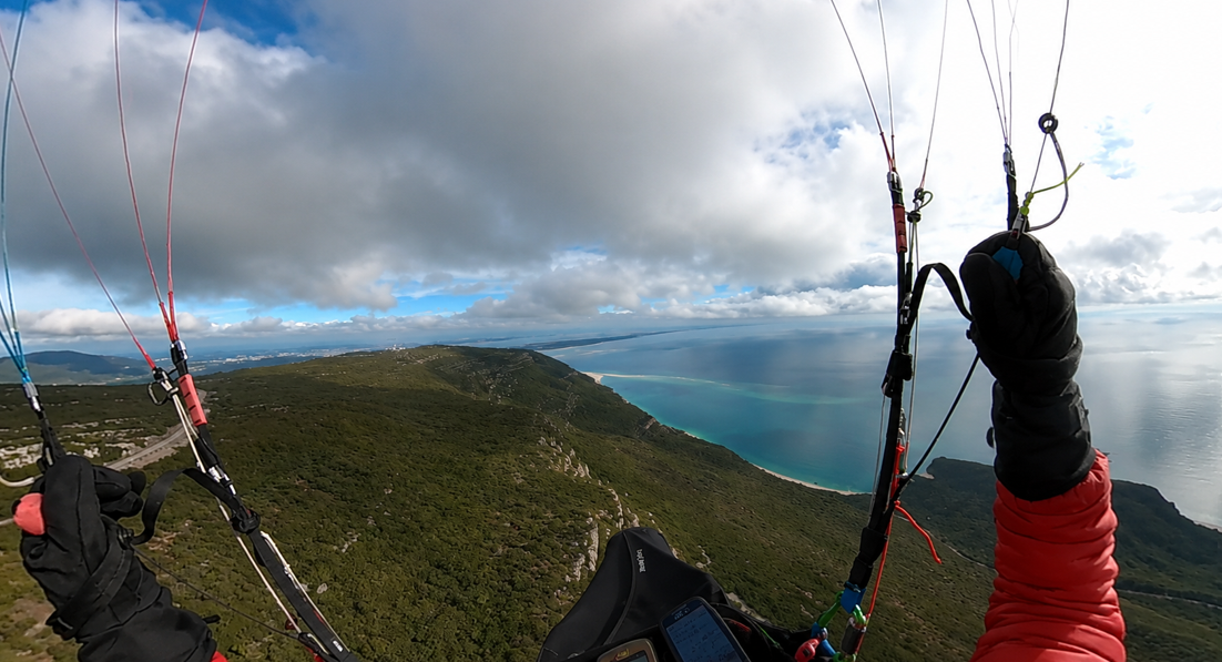 Paraglider soaring above the green Arrábida ridge and Atlantic bay, Portugal