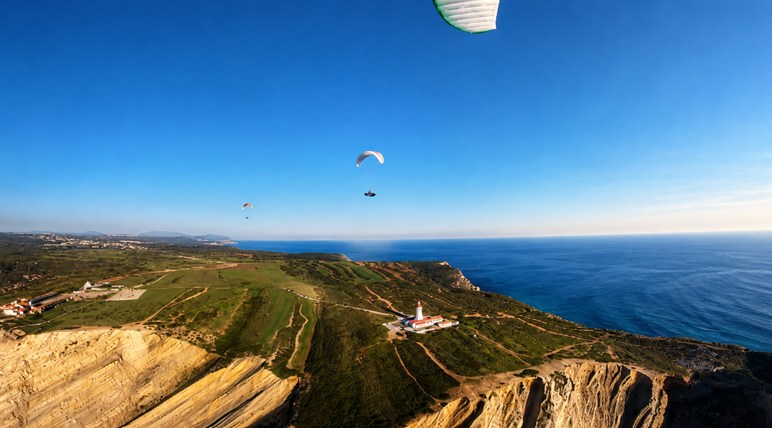Two paragliders soaring above Cabo Espichel lighthouse and Atlantic cliffs, Portugal