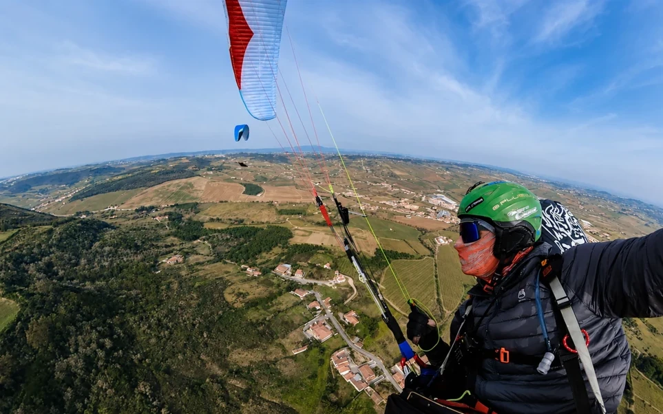 Cross-country paragliding coaching in inland Portugal: pilot in flight above green hills and farmland, with other paragliders nearby