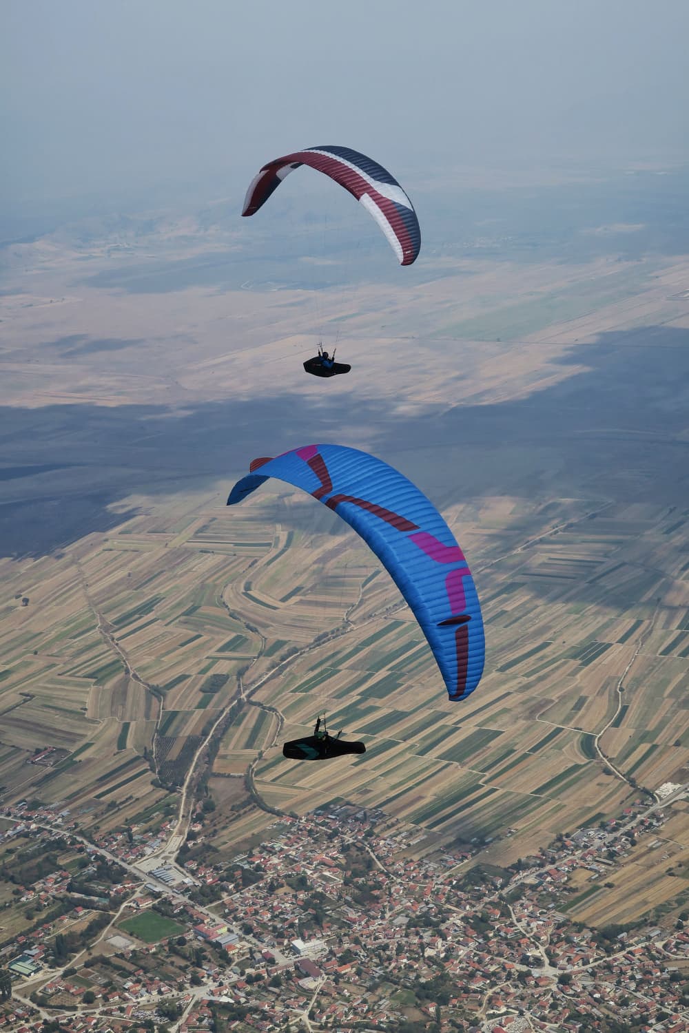 Two paragliders climbing in a thermal high above inland farmland